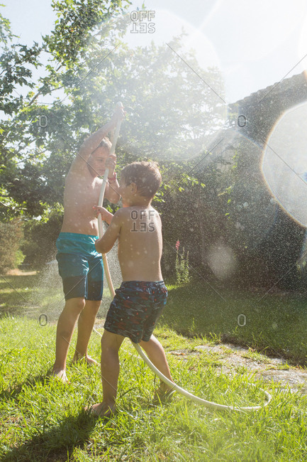 Little children in swimwear running around and splashing water from garden hose at each other