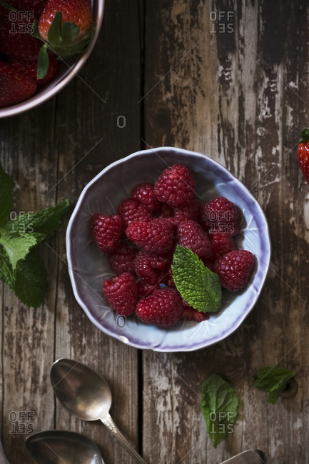 From above bowl with ripe strawberry and mint leaf placed on weathered wooden tabletop