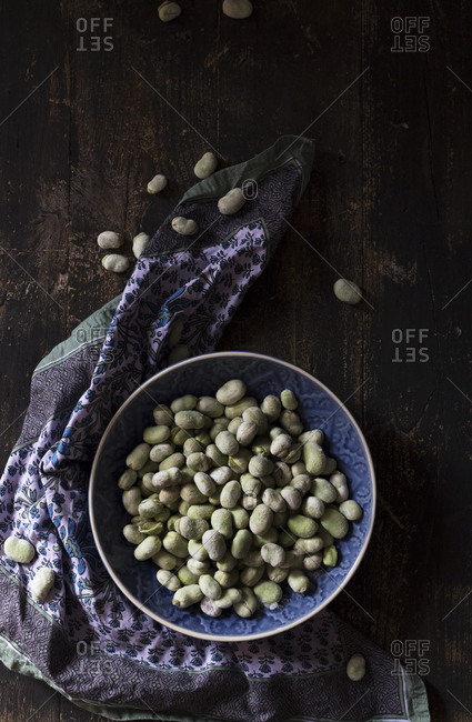 From above ornamental napkin placed near bowl with raw soy beans on dark lumber tabletop