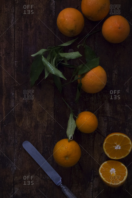 From above metal knife placed on dark wooden tabletop near cut and whole fresh juicy oranges