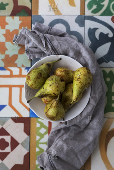 From above gray napkin placed near bowl with ripe pears on ornamental surface
