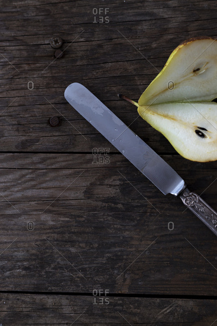 From above knife placed near halves of fresh ripe pear on wooden tabletop