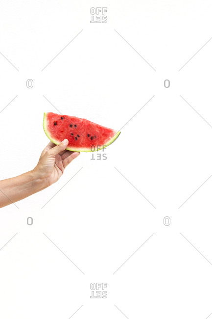 Hand of anonymous person holding piece of juicy sweet watermelon against white background