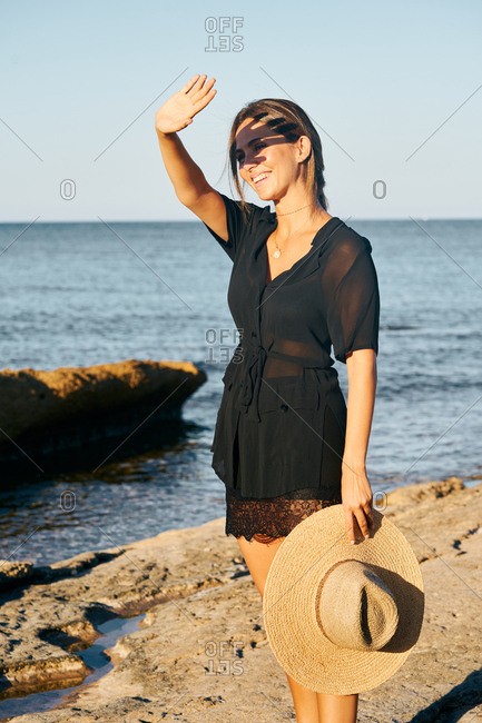 Young beautiful female model enjoying sun covering face from sun on beach holding hat