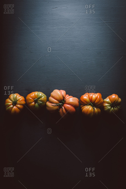 Heirloom tomatoes in a row on dark background