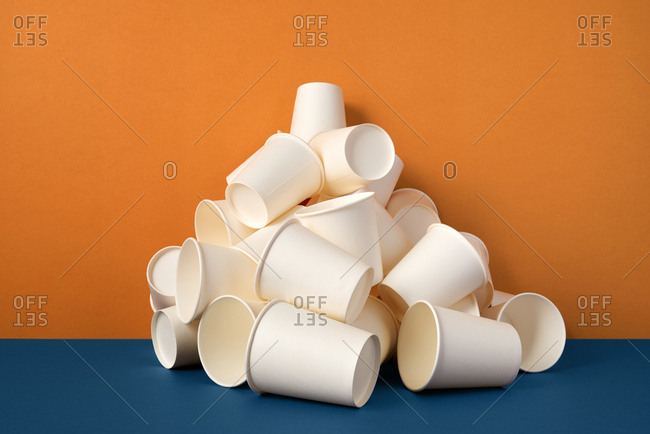 Stack of white paper drinking cups on orange and blue background.