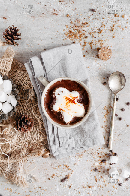 Gingerbread marshmallow on hot chocolate in a mug on a napkin with a metal spoon.