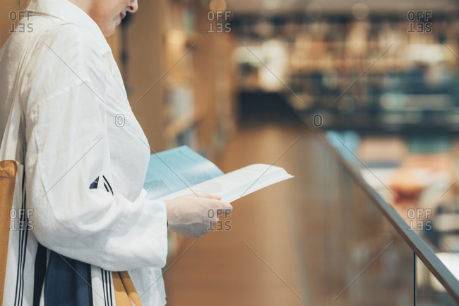 Unrecognisable woman reading a book at library.