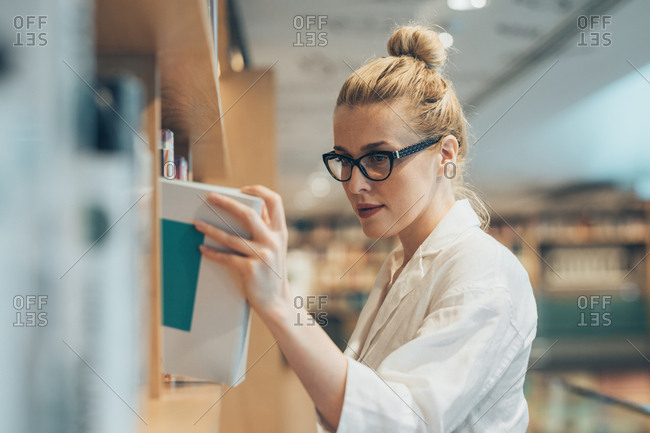 Pretty Caucasian woman picking a book from library shelf.