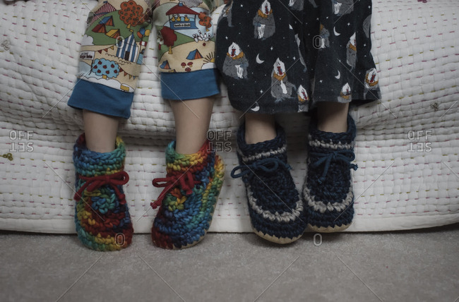 Low section of siblings wearing woolen shoes while sitting on bed at home