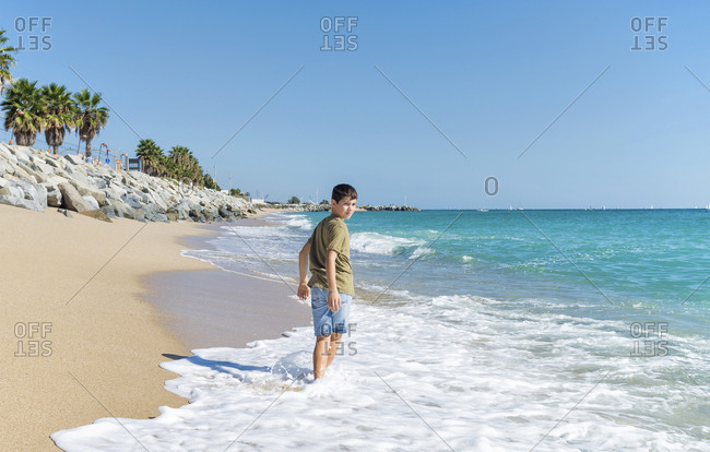 Rear view of young boy barefoot  walking on seashore in sunny day