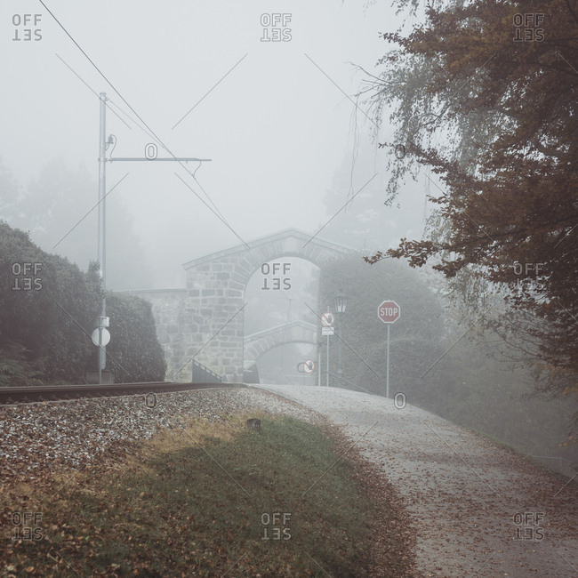 Road leading towards archway against sky during foggy weather