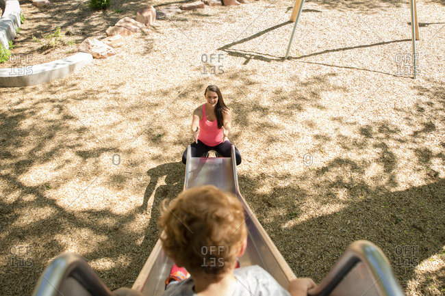 High angle view of son sliding while mother crouching by slide at playground
