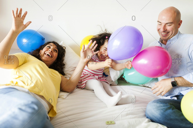 Happy family playing with colorful balloons on bed at home