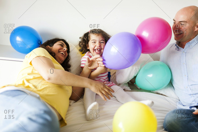 Happy parents with daughter playing with colorful balloons on bed at home