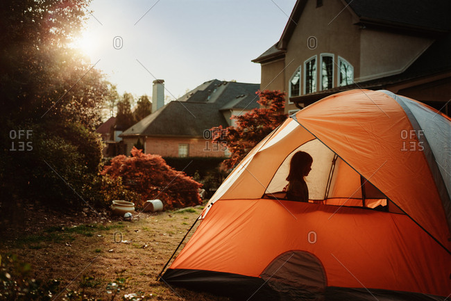 Silhouette of little girl in tent while camping in backyard