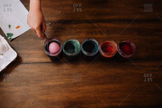 Child dyeing Easter eggs on wooden table