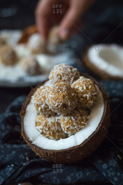Raw coconut balls in halved coconut with human hand in background making coconut balls