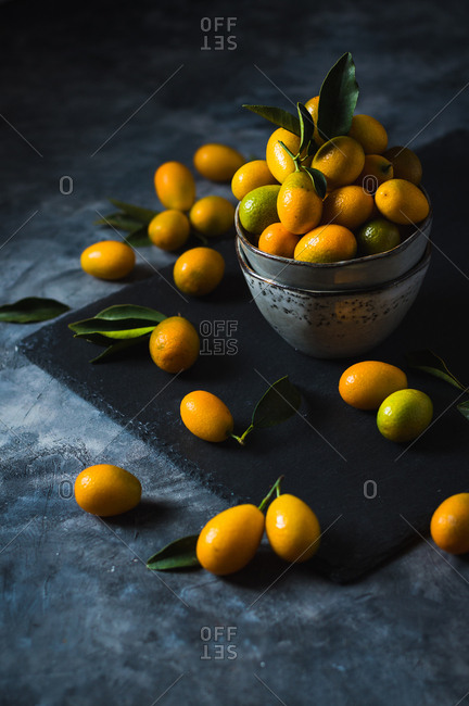 Freshly picked kumquats in grey modern bowl on dark surface