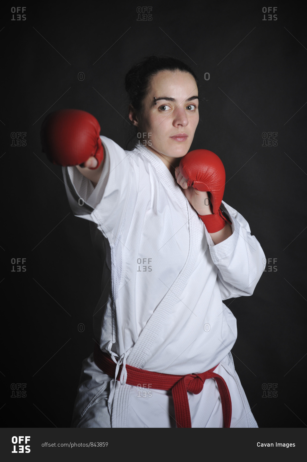 Portrait of woman wearing boxing gloves while practicing karate against black background