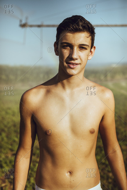 Boy cooling off with farm sprinklers in a field of corn