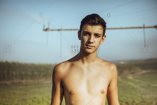 Boy cooling off with farm sprinklers in a field of corn
