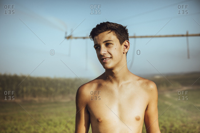 Boy cooling off with farm sprinklers in a field of corn