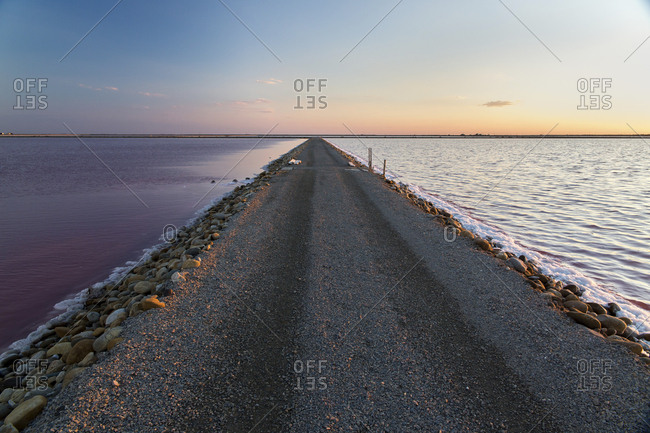 Empty road amidst salt flats against sky during sunset