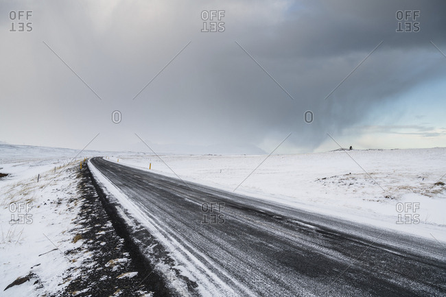 Empty road amidst snow covered landscape against cloudy sky