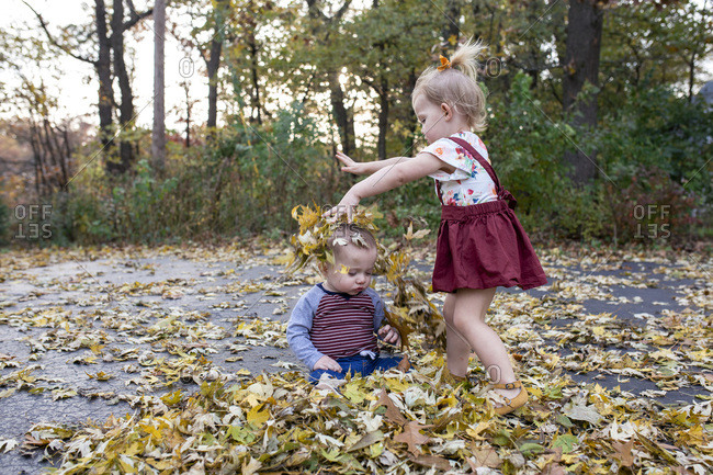 Toddler girl throwing colorful leaves on little brother