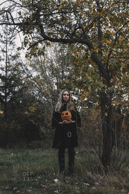 Young woman holding jack o' lantern while standing in forest during Halloween