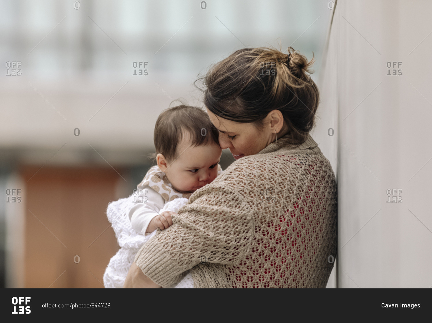 Mother comforting her baby while leaning against wall