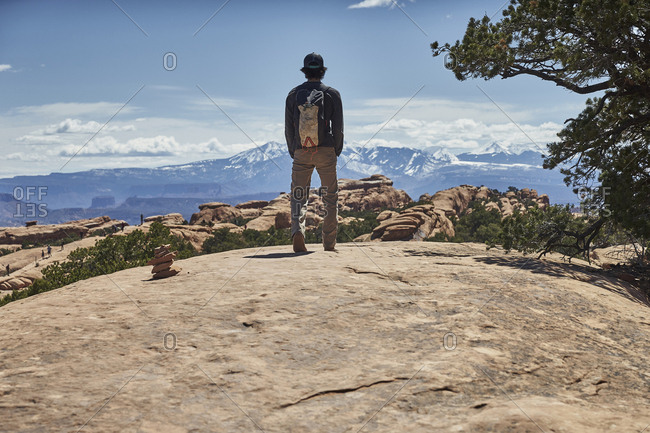 Rear view of male hiker with backpack looking at view while standing on mountain against sky during sunny day