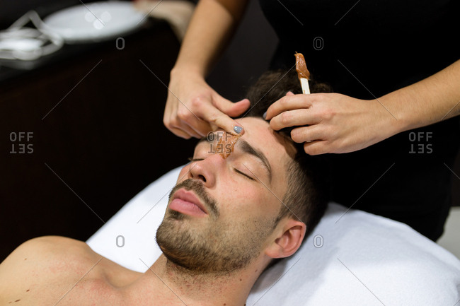 Relaxed young man is getting eyebrow waxing at beauty salon