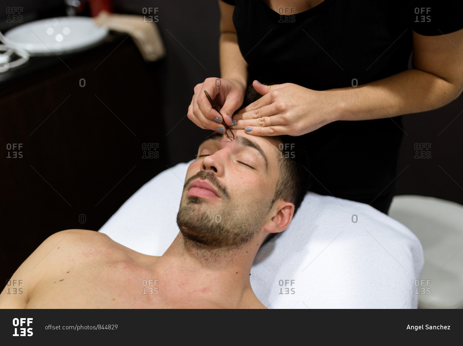 Relaxed young man is getting eyebrow waxing at beauty salon