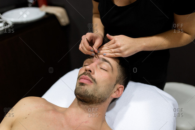 Relaxed young man is getting eyebrow waxing at beauty salon