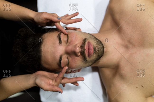 Overhead view of young man is getting facial massage by a cosmetician in a beauty spa