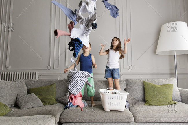 Siblings standing on the couch throwing laundry in the air