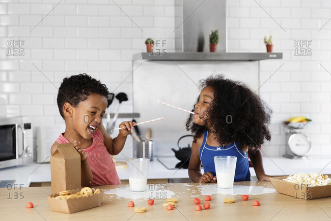 Siblings playfighting with drinking straws in the kitchen
