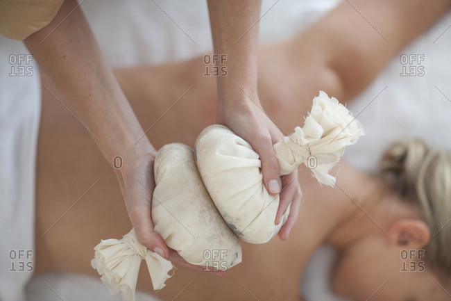 Masseuse holding aromatherapy sachets over woman's back