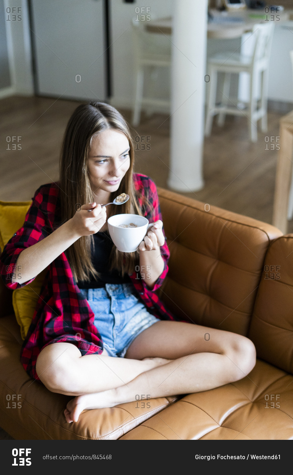 Relaxed young woman eating cereals in living room at home