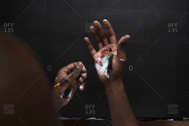 Dirty hands of artist with colorful paints against black background