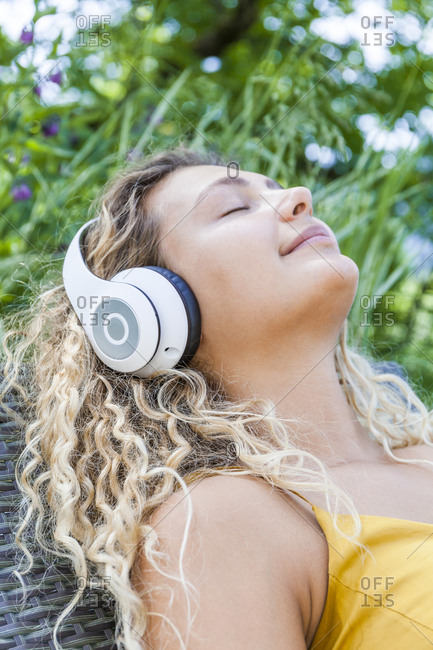 Smiling woman listening to music with closed eyes- lying on deckchair