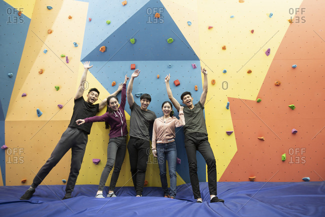 Happy young Chinese friends standing against climbing wall at gym