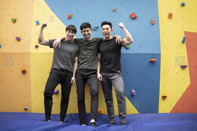 Happy young Chinese men standing against climbing wall at gym