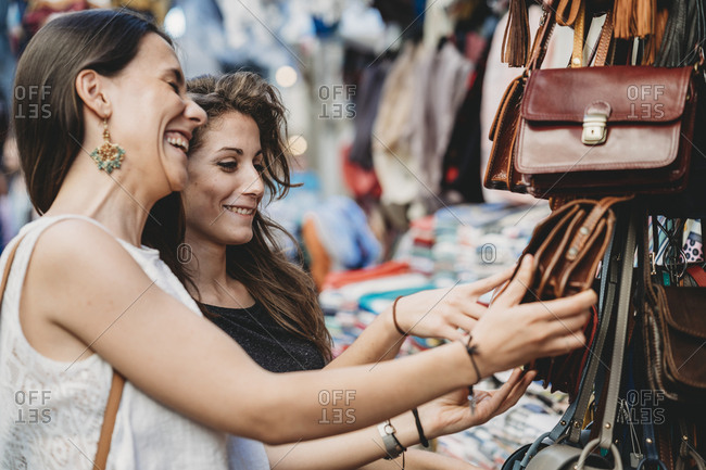 Happy female friends buying purse at market