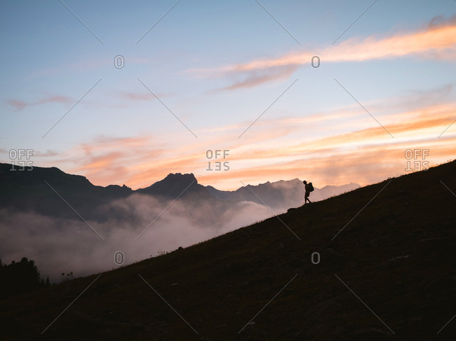 Silhouette of hiker walking down a mountain at sunset