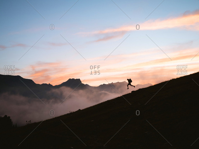 Silhouette of hiker walking down a mountain at sunset