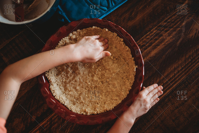 Girl's hands pressing down pie crust into dish at table