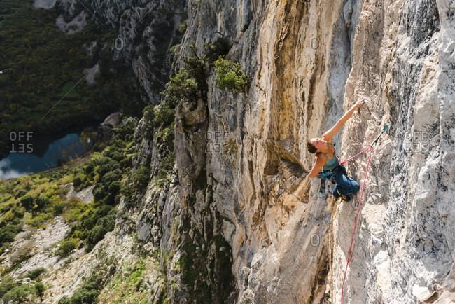 Strong woman rock climber resting from a ledge in vertical wall